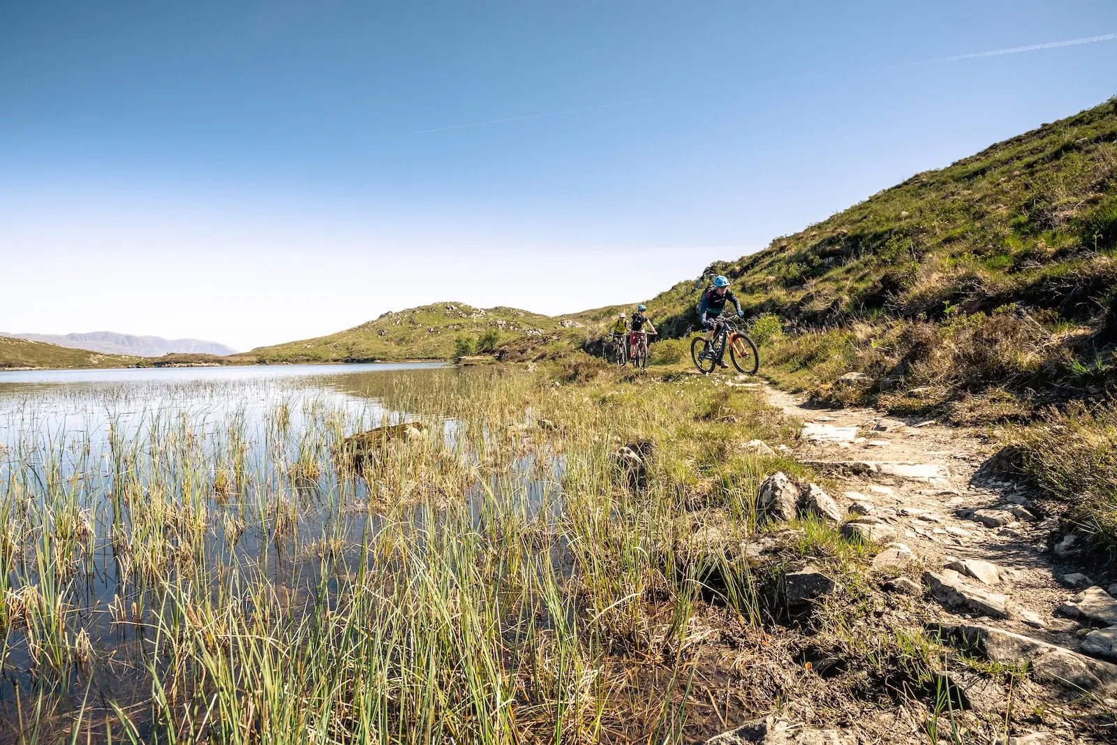 Mountain bikers riding around a loch in Scotland